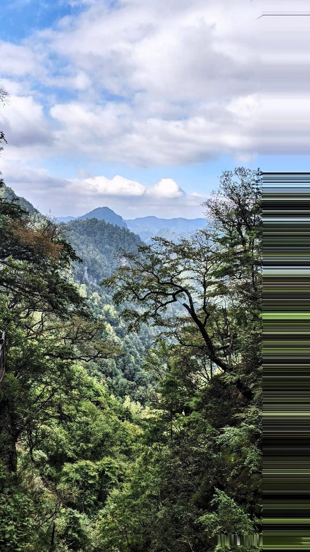 峭壁巍峨耸立，漫山草木郁郁葱葱，远处层叠的山峦在云海之下若隐若现。天上云