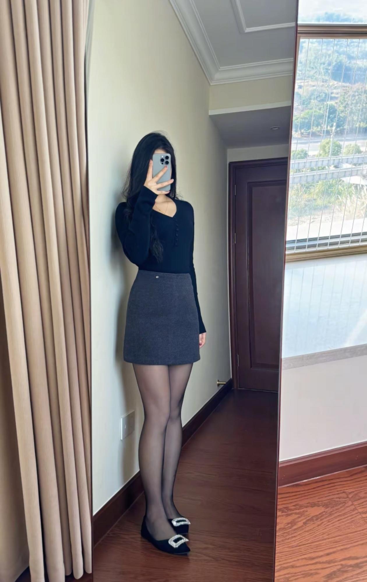 穿着黑色上衣和灰色短裙，搭配黑色丝袜和鞋子。