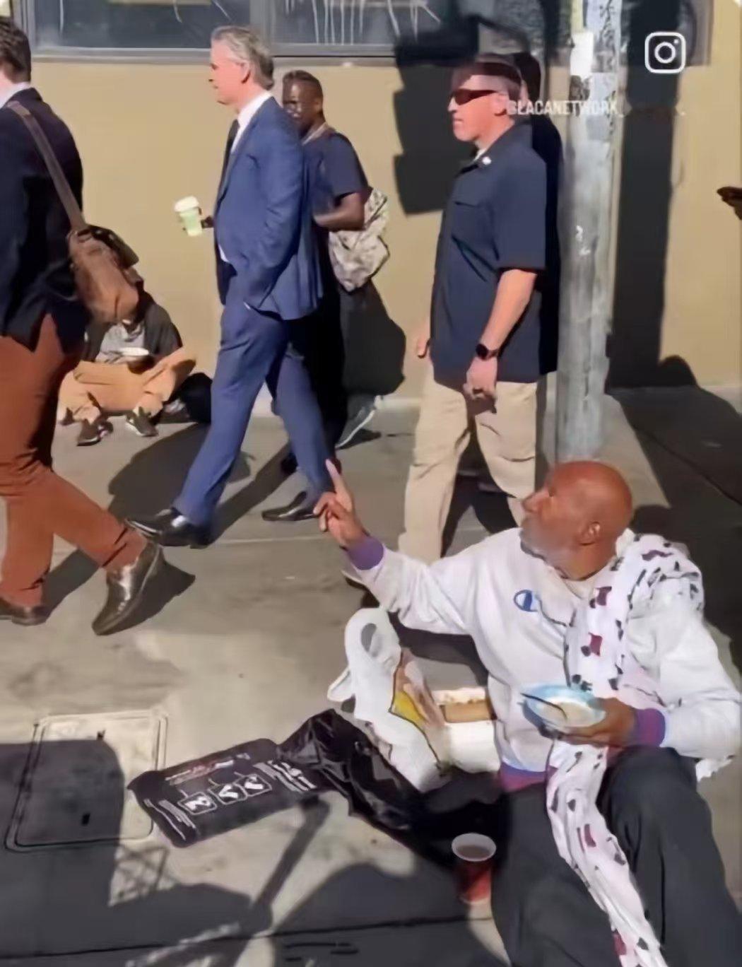 世界名画加州州长纽森单手插兜，在保镖簇拥下从美国流浪汉身边淡然走过，手里还拿着一