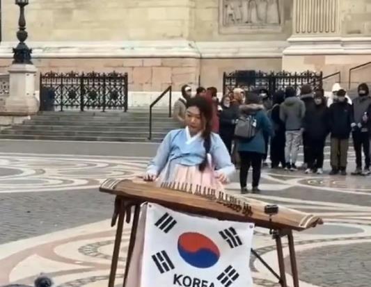 韩国对古筝下手了，一位身着韩服的女子在伦敦考文特花园弹奏古筝，乐器下方悬挂的韩国