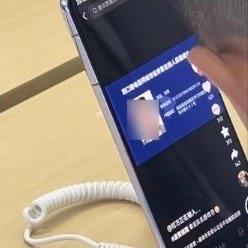 一男孩站在展示台前，左手举着显示通缉令的手机，右手在另一台试用机上飞速输入逃犯的