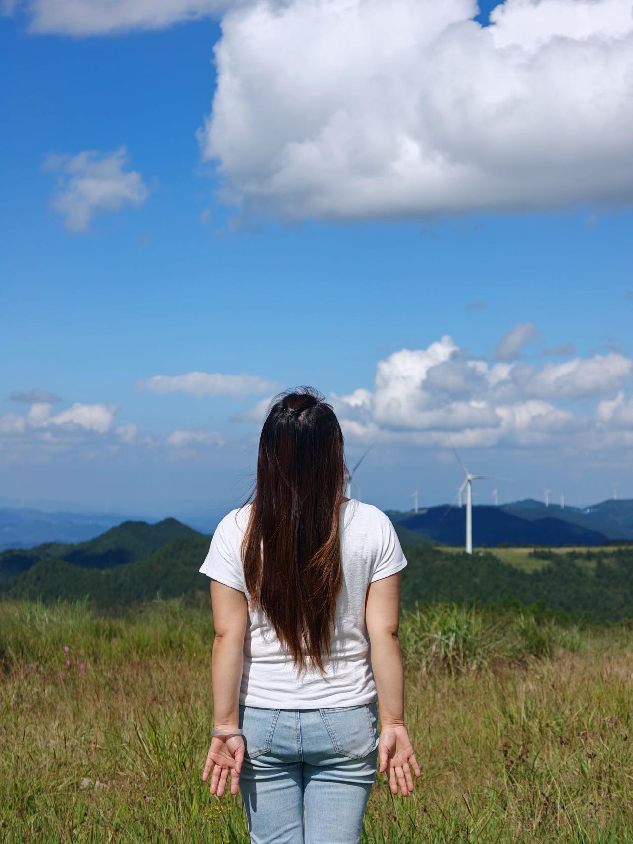 站在辽阔的山野之巅，任由山间的清风拂过，望着远处连绵群山与缓缓转动的风车，蓝天白