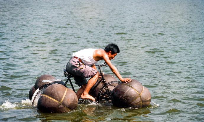 这是1983年9月杭州，一名男子正骑着自己设计的水陆两栖自行车渡河。男子在自行车