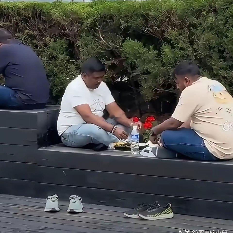 上海外滩，几个印度游客逛饿了直接在观景台花坛边脱鞋，盘腿铺开食物用手抓着吃，吃完