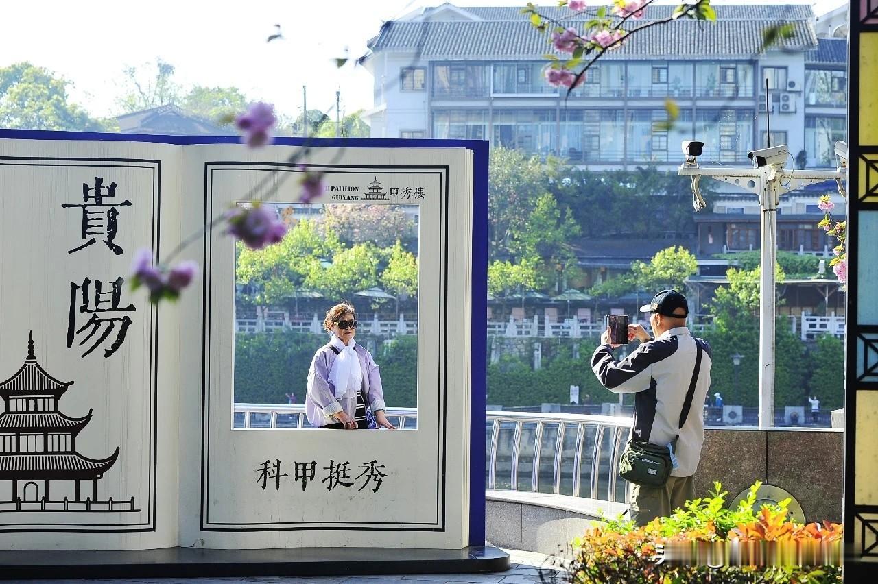 贵阳：外地游客在甲秀楼景区打卡春暖花开，南明河畔河水潺潺流动，柳絮在微风吹拂