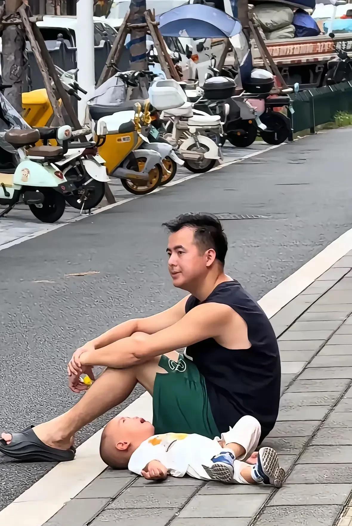 图片中这位男子，带孩子出去玩，感觉自己累了，就在路边就地坐下来休息。可是炎炎夏