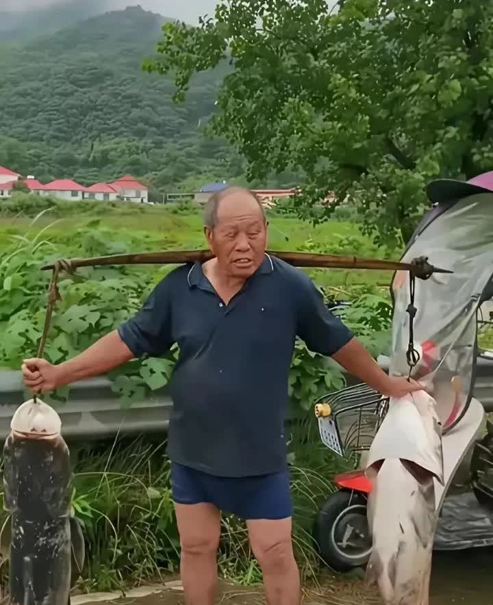 湖南一男子开车路过村道时，发现一大叔挑着两条大头鱼，每条鱼都得有30斤，便停下车