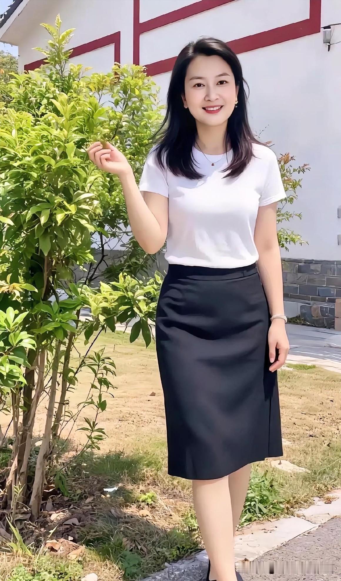 白衣黑裙简约大方，绿树红墙映笑颜。清新自然，尽显优雅从容。