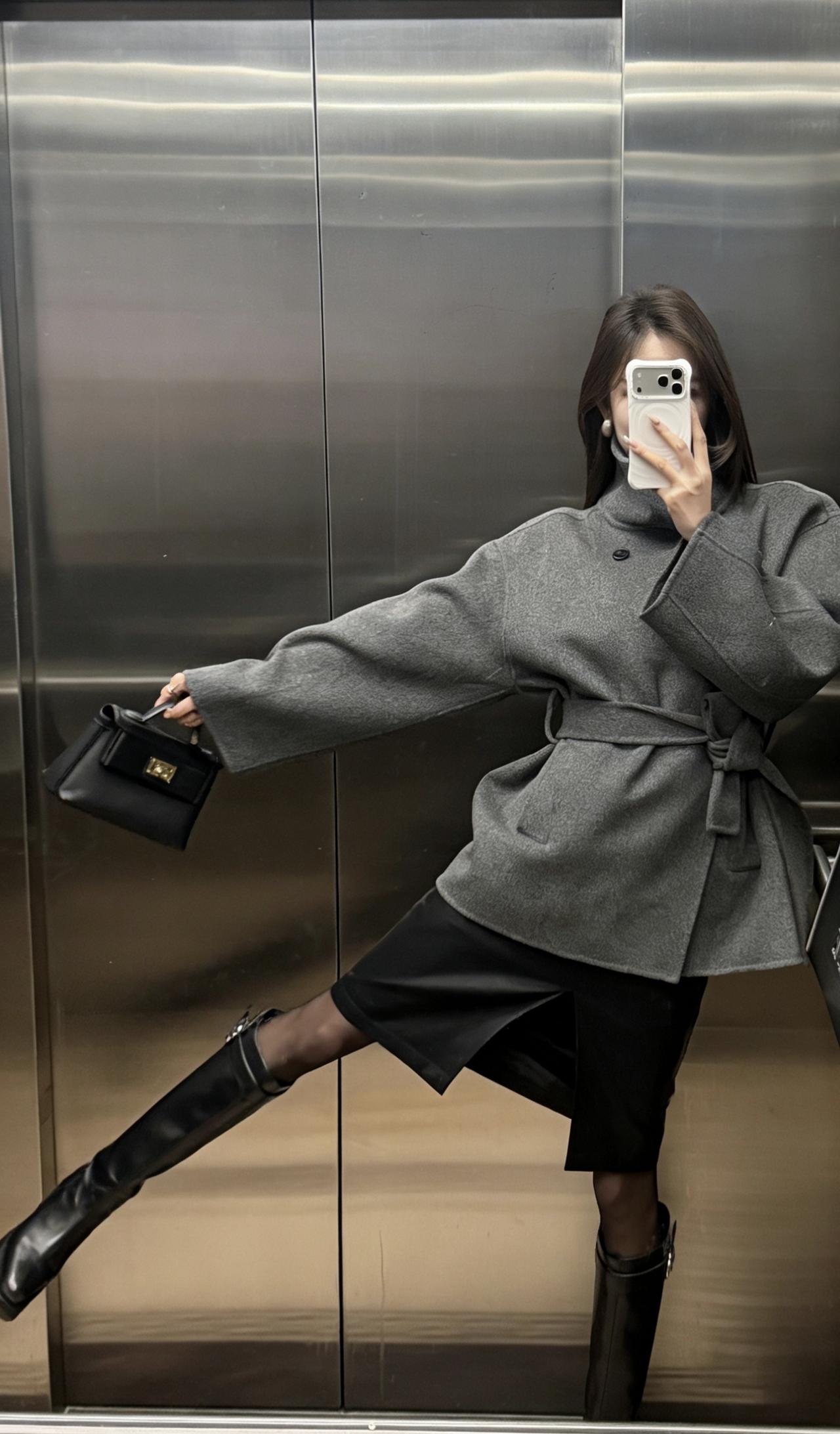 今日穿搭推荐：灰色收腰毛呢短大衣为主打，搭配黑色开叉皮裙、黑丝与黑色长筒靴，手持