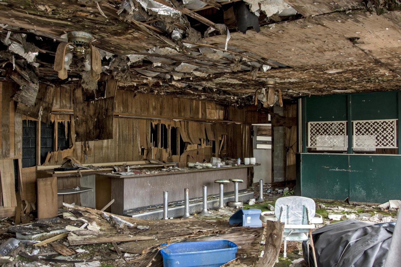 这是美国肯塔基州75号州际公路旁一家废弃餐厅的内部景象，桌椅散乱，墙壁剥落。风扇