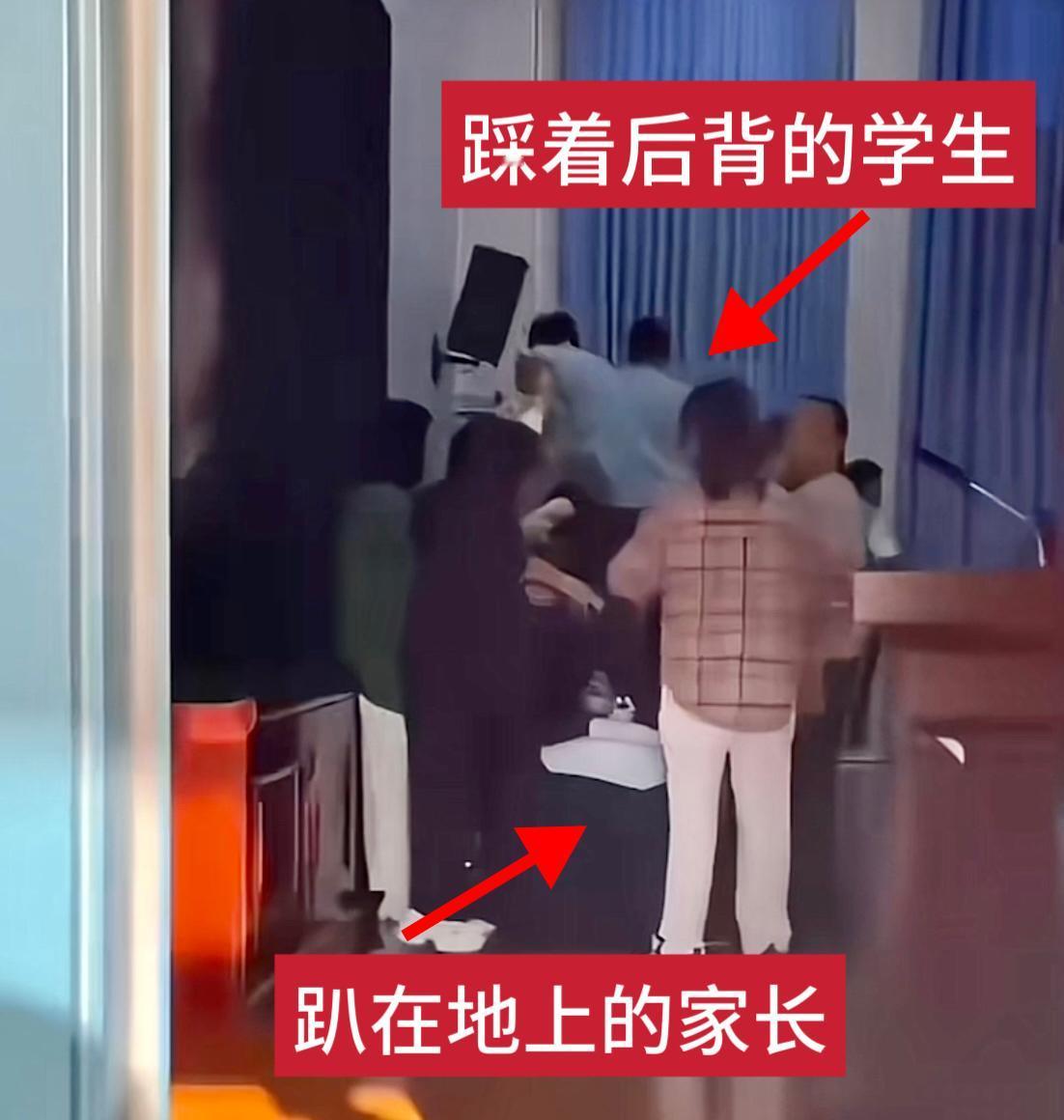 一排家长趴在地上、一队学生踩在家长的后背从一侧走到另一侧、现场还有人用话筒喊着“