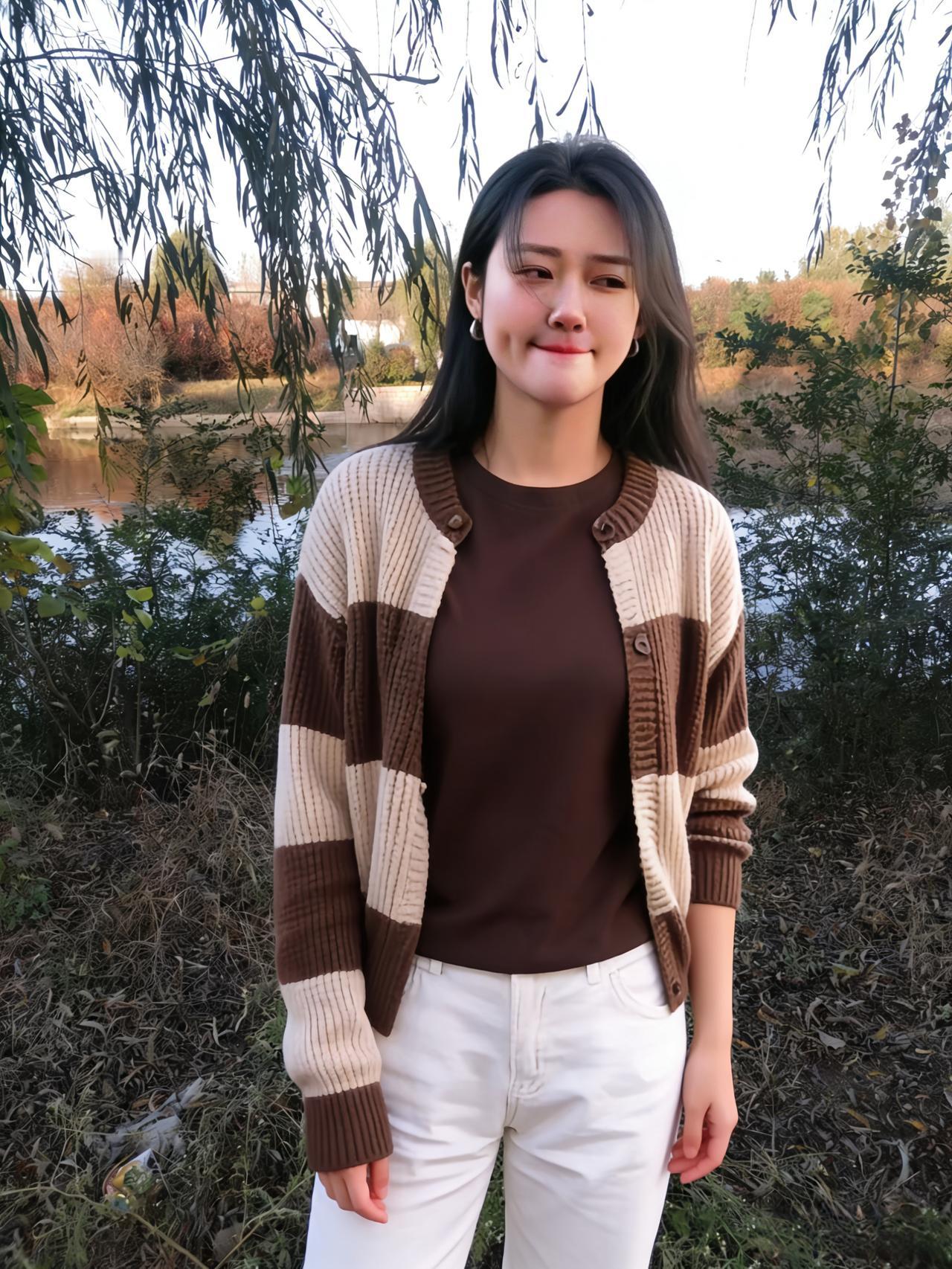 柳岸晴光映丽人，棕衫白裤衬清新。开衫格纹凝秋韵，笑靥明霞染绛唇。河水粼粼摇碎