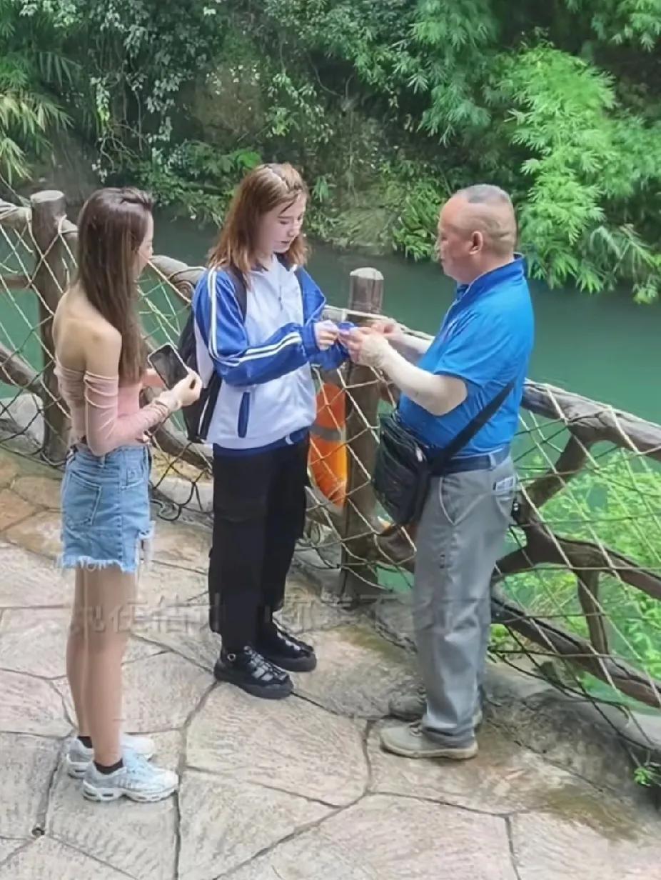 两个女孩站在景区的瀑布前拍照时，一位老人站在不远处一直盯着女孩看，一个女孩气冲冲