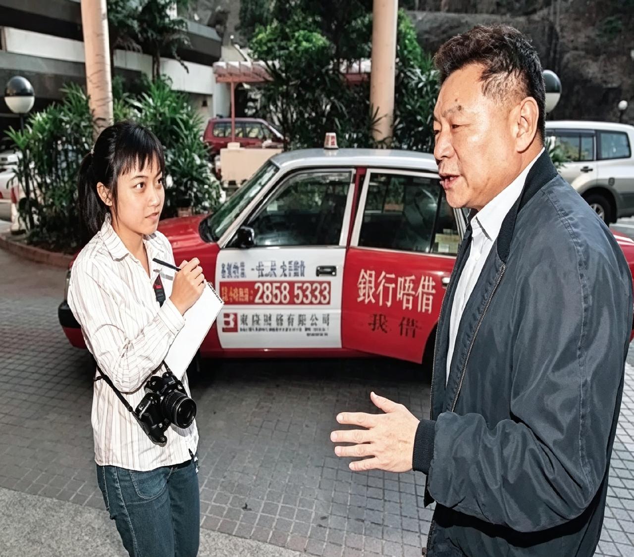 2000年街头，甘比还是个拿本子采访的小记者，旁边刘銮雄正比划着说话。背景出租车