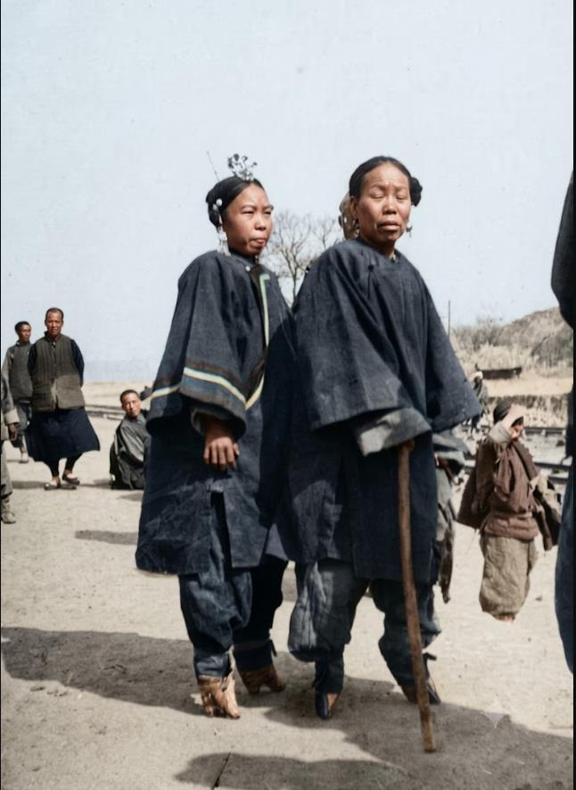 清末，城郊街头，两位缠足汉族女性结伴出行。两位女性身着宽边大襟长袄、束口长裤，