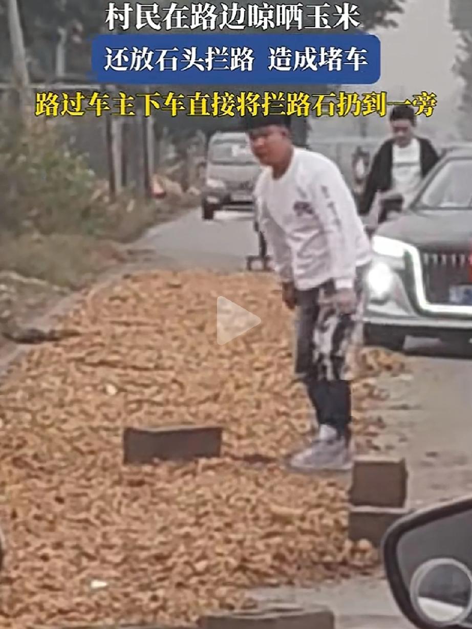 村民在路边晾晒玉米，还放石头拦路造成堵车，这时一位路过的年轻小伙下车后直接将“拦