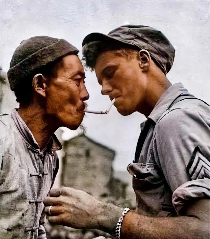 二战期间，一名美国大兵正在向一名中国劳工借火。这名大兵身穿军装，头戴军帽，叼着一