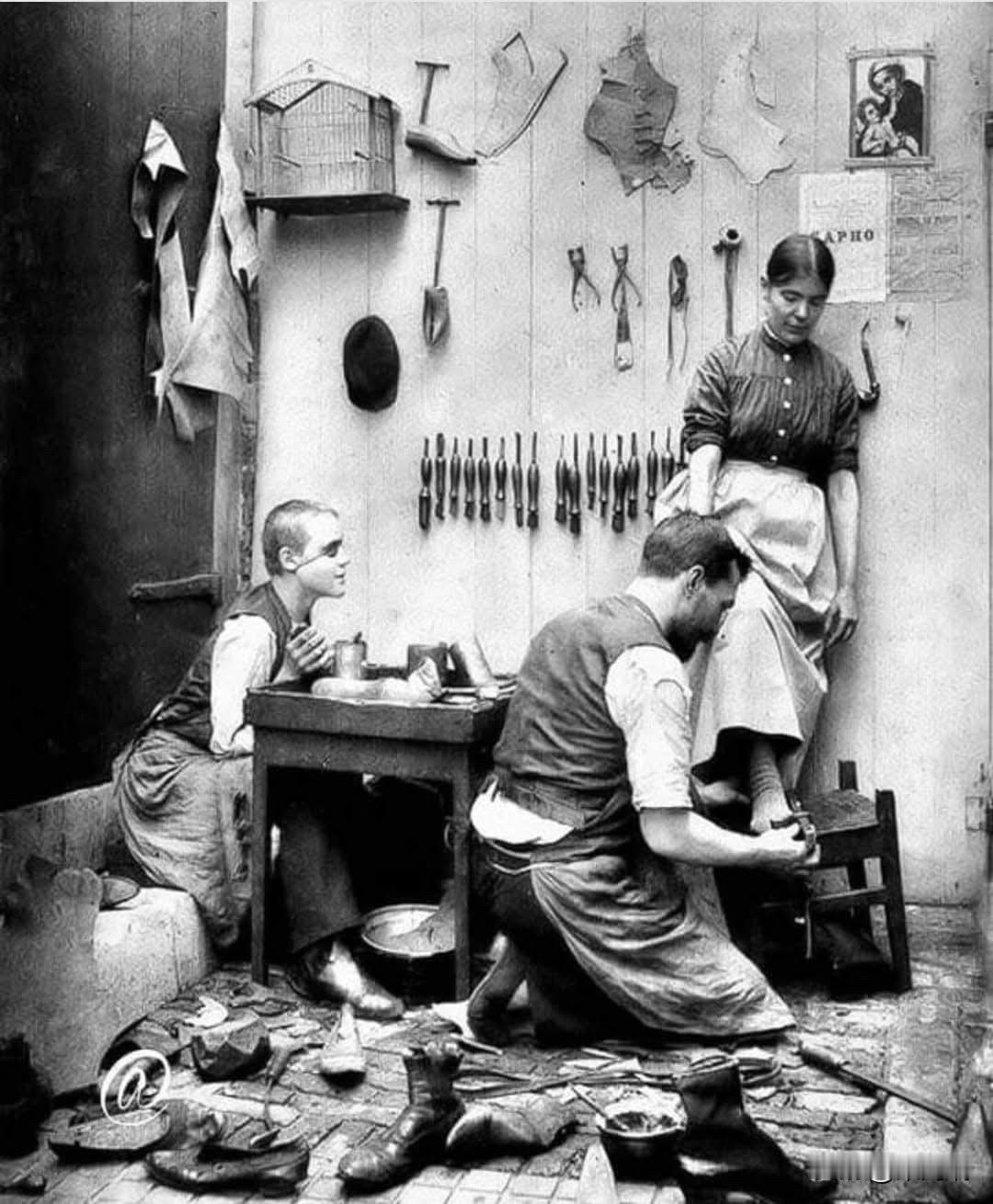 这张图片展示了19世纪（约1880年代）法国的一家鞋匠铺。画面中有一名