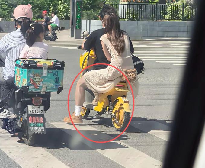 一名长发飘飘、穿着长裙的女子坐在男友的小电驴后座上，谁料连衣裙底下竟露出一双粗壮