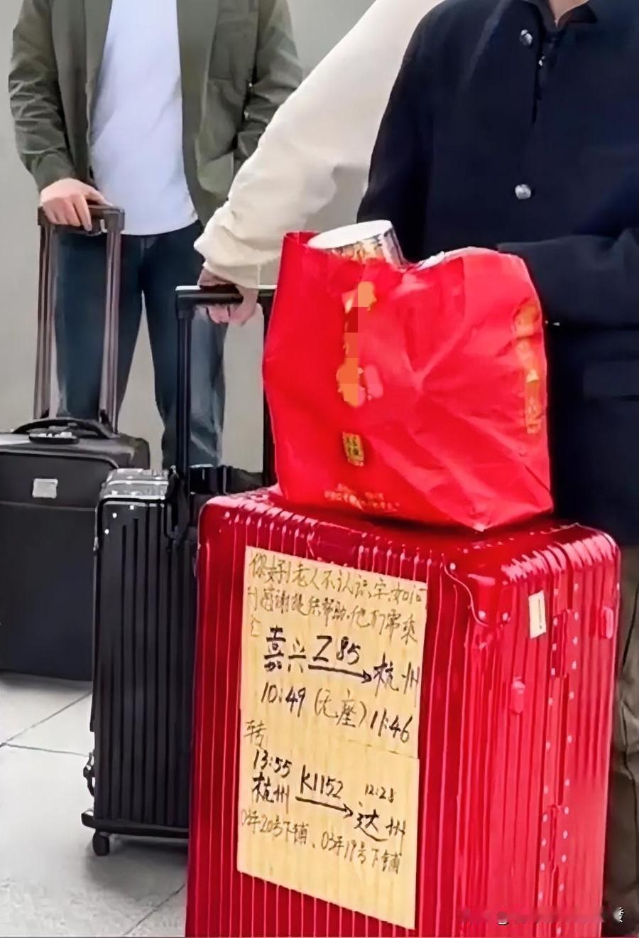 火车站内，一位戴口罩的老人独自等车，其前面放着一个特别红的行李箱，箱子上面还摆着