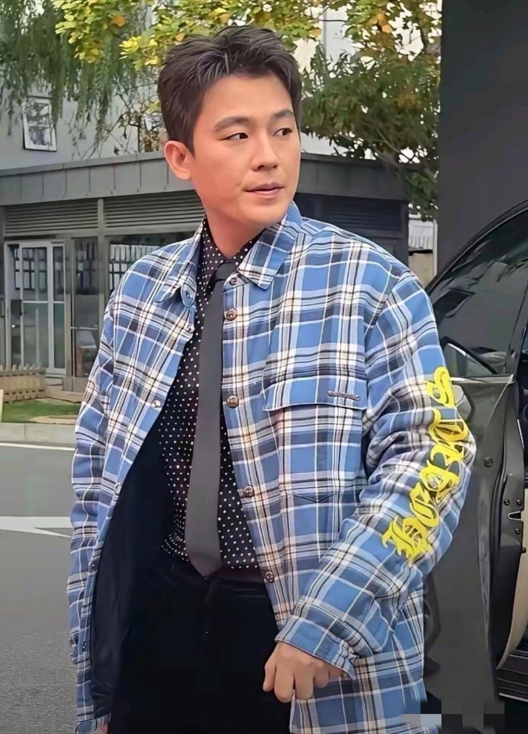 画面中的欧豪肤色偏黄，银丝醒目，脸型狭长，法令纹清晰，衣品欠佳，黑色波点衬衫外居