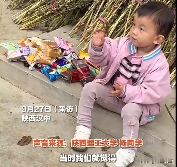 陕西，一位3岁小女孩坐在自家门口玩耍，这个时候看到一群来乡间拉练军训的大学生。小