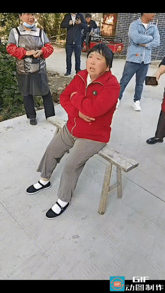 安徽阜阳，一队婚车从村里道路穿过，被一名大妈拦路截停。大妈搬来一条板凳，正正地