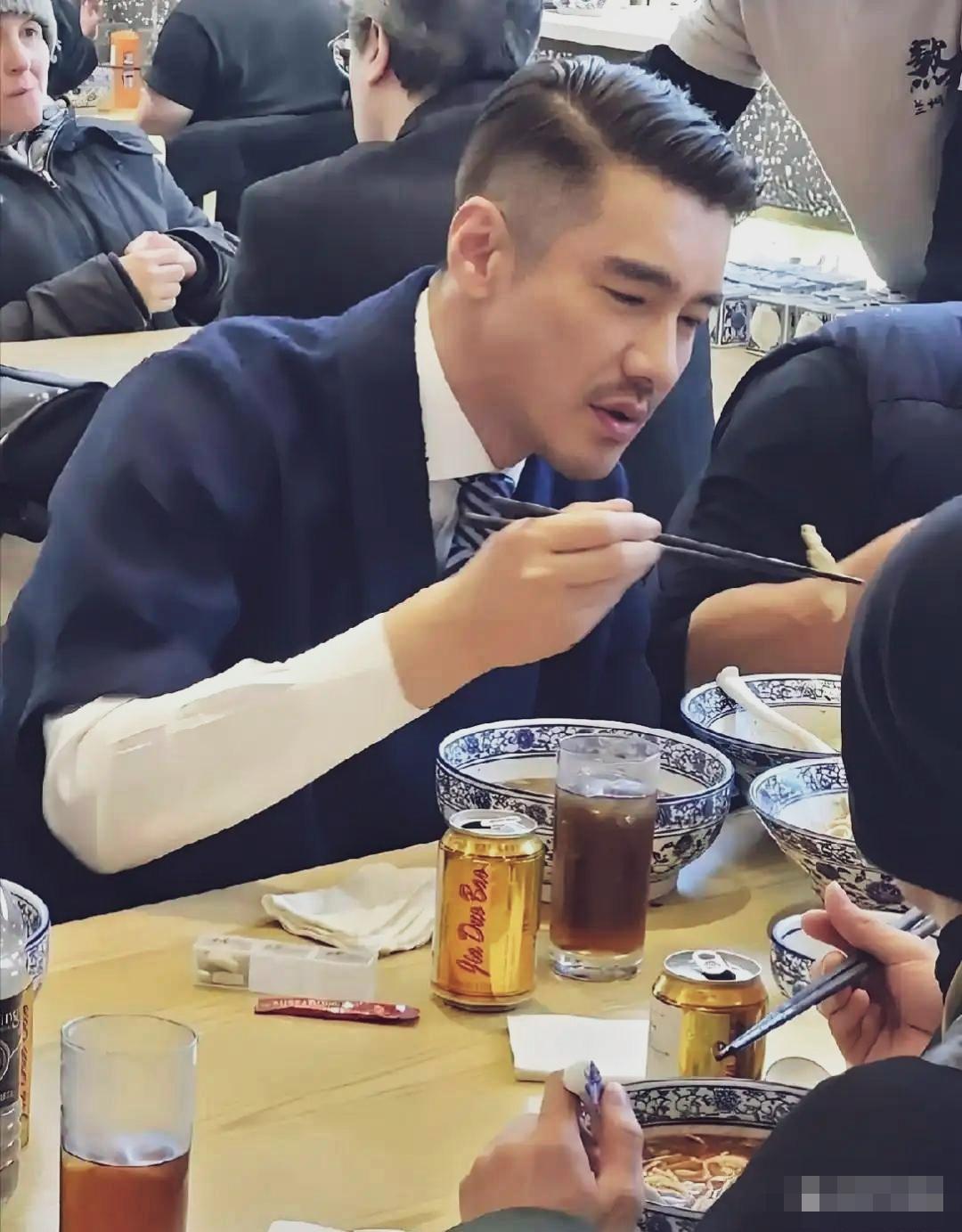 胡兵，利落侧分油头，西装马甲配领带，一身精致正装，坐在面馆嗦面，氛围感反差感十足