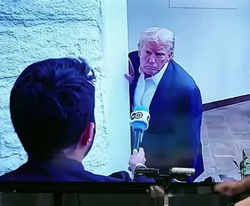 记者拿着话筒要采访特朗普，从画面看特朗普露出半侧身，手扶着墙，表情严肃。这幅画面