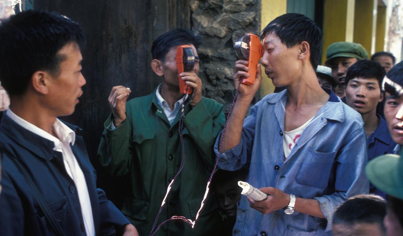 1980年，昆明街头围着一群人。其中两个男子，手里拿着奇怪的东凑近眼睛仔细看，一