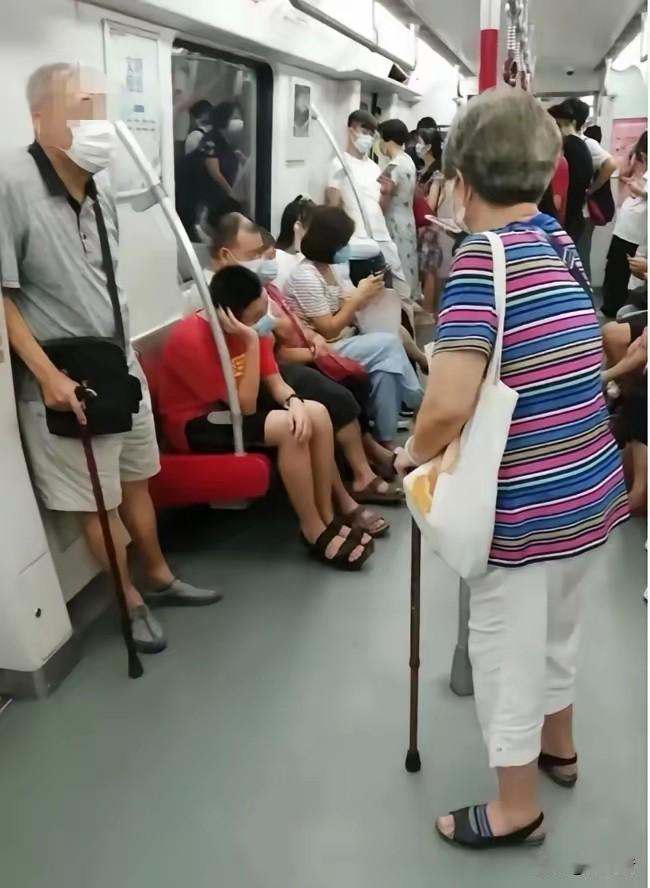 地铁上两位老者拄着拐棍站在那里。旁边年轻人在座位上坐着，有的扭着头、有的看手机装
