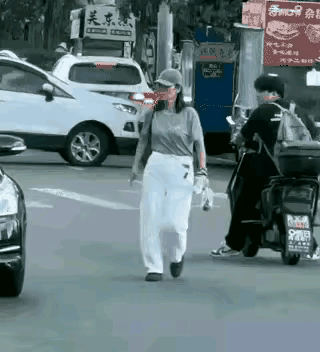 一名女子慢悠悠走在马路正中间，对身边驶过的车辆毫不在意。看到一辆小车靠近时，她突