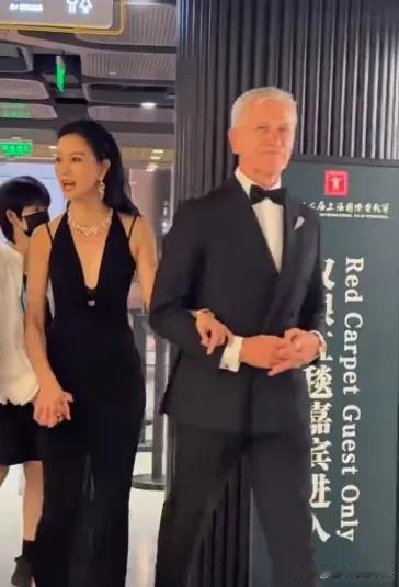 女星倪虹洁手挎帅老外胳膊一起走红毯，一袭黑色礼服长裙，身材高挑丰满，脖子上金光闪