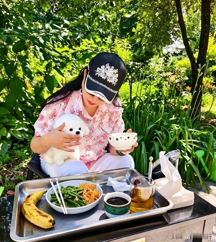 这画面好养眼啊！76岁的刘晓庆坐在自家小院露天吃饭，怀里搂着可爱的小白狗，一只手