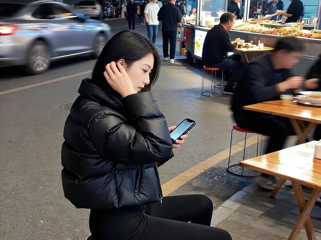 夜市边的黑与暖夜晚的街边，车流碾过路灯的光她踩在石墩上，举着手机对着夜色