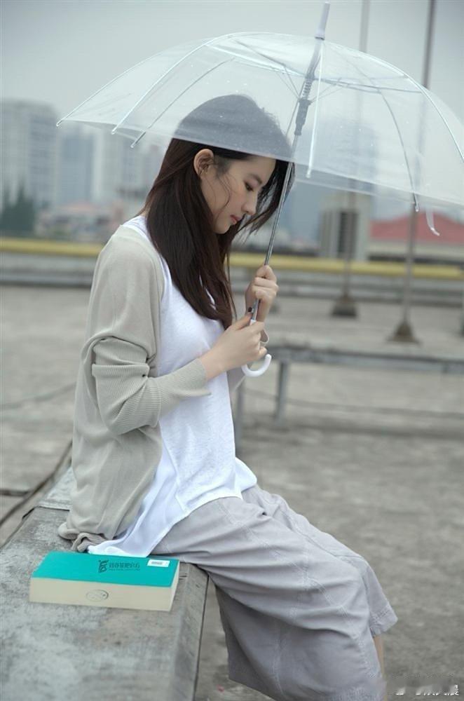 阴雨天里，刘亦菲撑伞捧书而立，雨丝朦胧间，那份清纯文艺的气质悄然流露，画面格外动