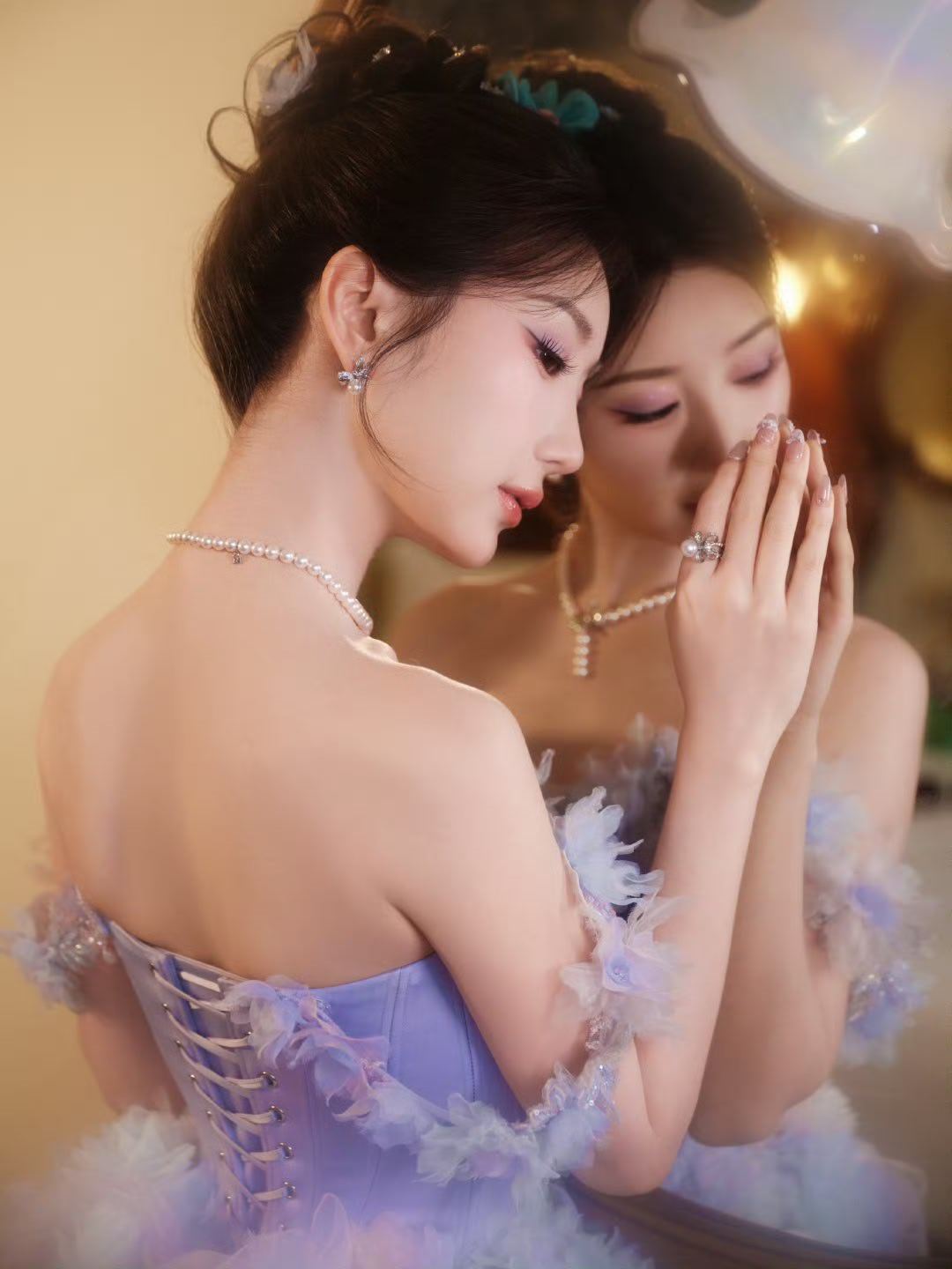 她身着淡紫渐变礼裙，裙身缀满柔纱花饰，露肩设计衬出纤柔肩颈，珍珠项链添了几分贵气