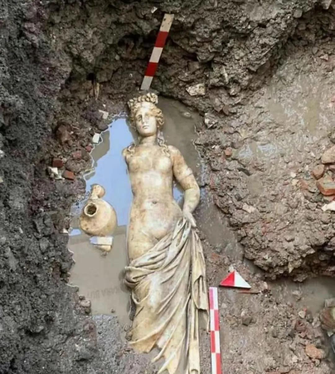 土耳其阿马斯拉出土的古罗马美女雕像，半掩于泥土中，四周散落着测量工具和挖掘痕迹。