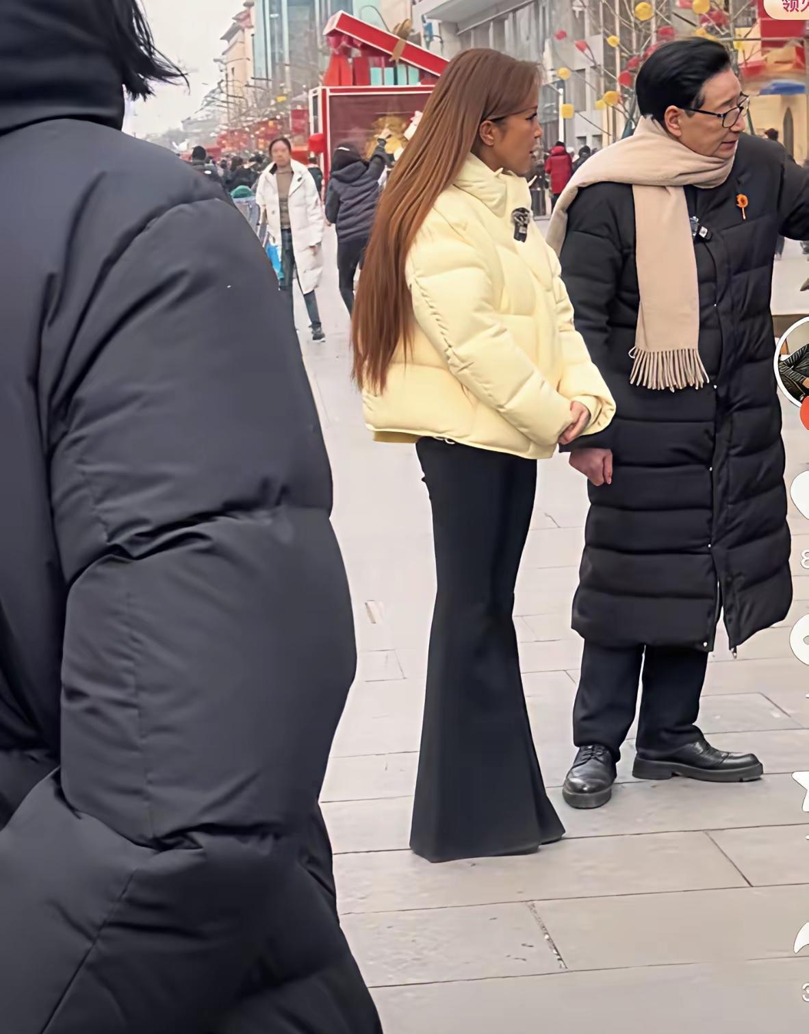 春晚“定海神针”素颜逛王府井，细纹里夹着风。米色面包服+喇叭裤，她连口红都没补