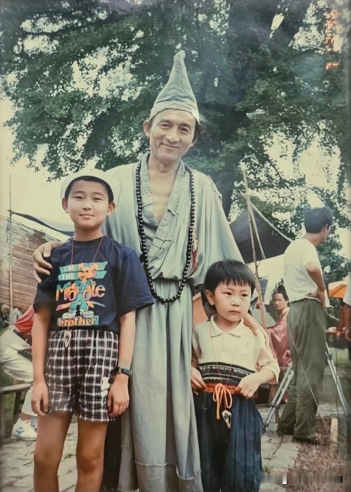 这是游本昌老师身着济公戏服，在大树下和两个小朋友的合影。当年《济公》火遍大江南北
