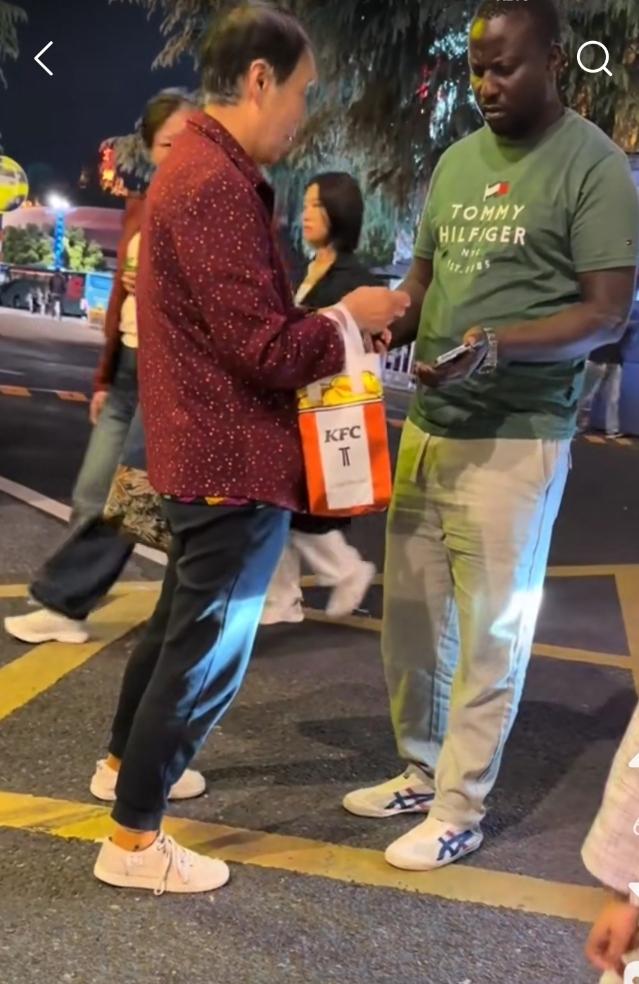 某地街头，一大妈正在交易。街头上虽人来人往，也丝毫不影响他们的心情。都七老八