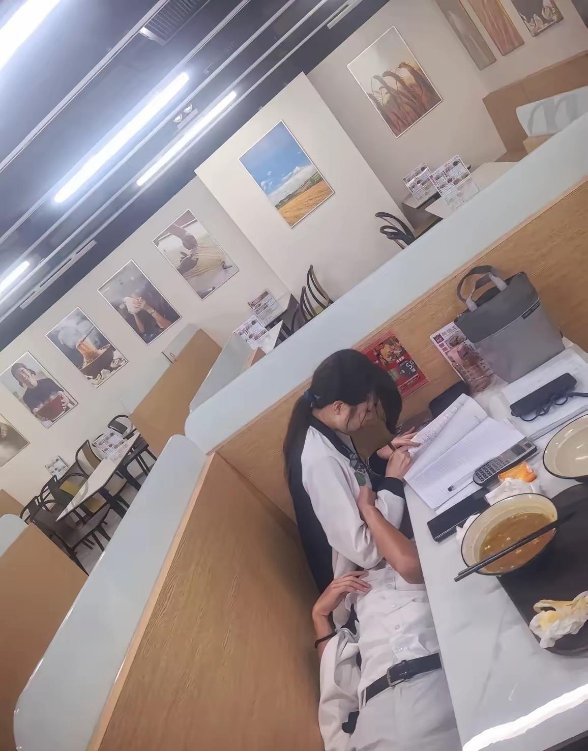 食堂喧嚣嘈杂，人声与餐盘碰撞声此起彼伏。男生安心枕在女孩腿上，闭目休憩，卸下一