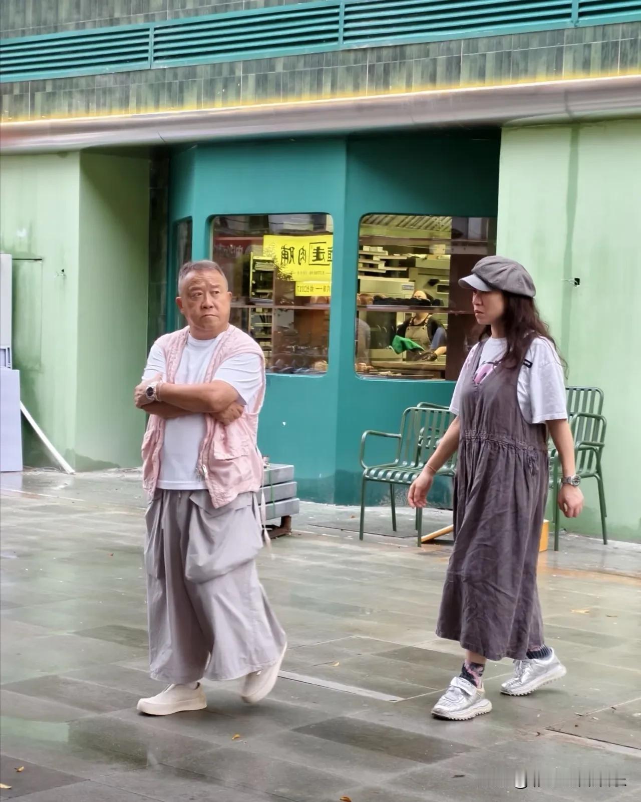 曾志伟和女友出街，一身打扮很引人注目，曾志伟穿着粉色马甲搭配阔腿裤，阔腿裤上有两