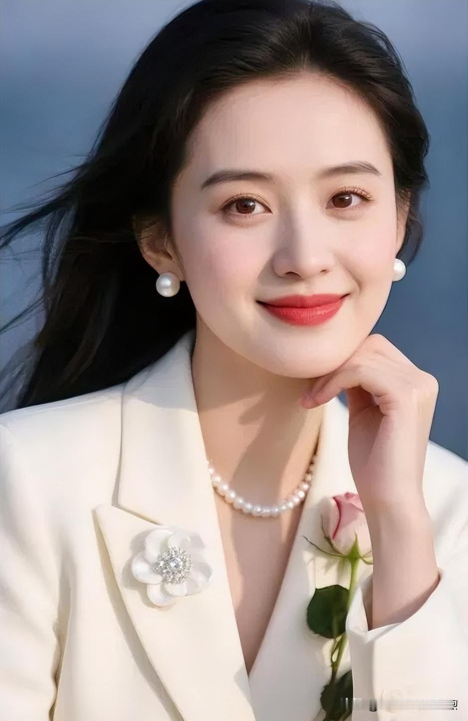 微风轻拂，发丝微扬。温婉笑靥，凝眸生辉。一袭白衣清雅，珍珠点缀锁骨，手捧娇艳玫瑰