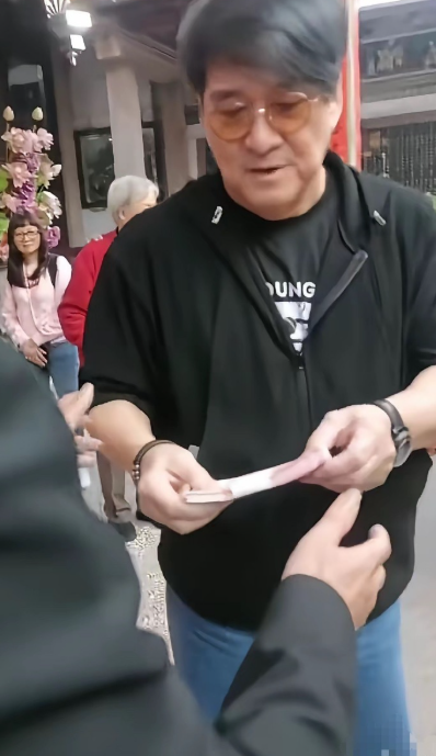周华健满脸堆笑拿出一W块钱并交代着什么给周氏祠堂主事人，周围人露出难以置信表情，