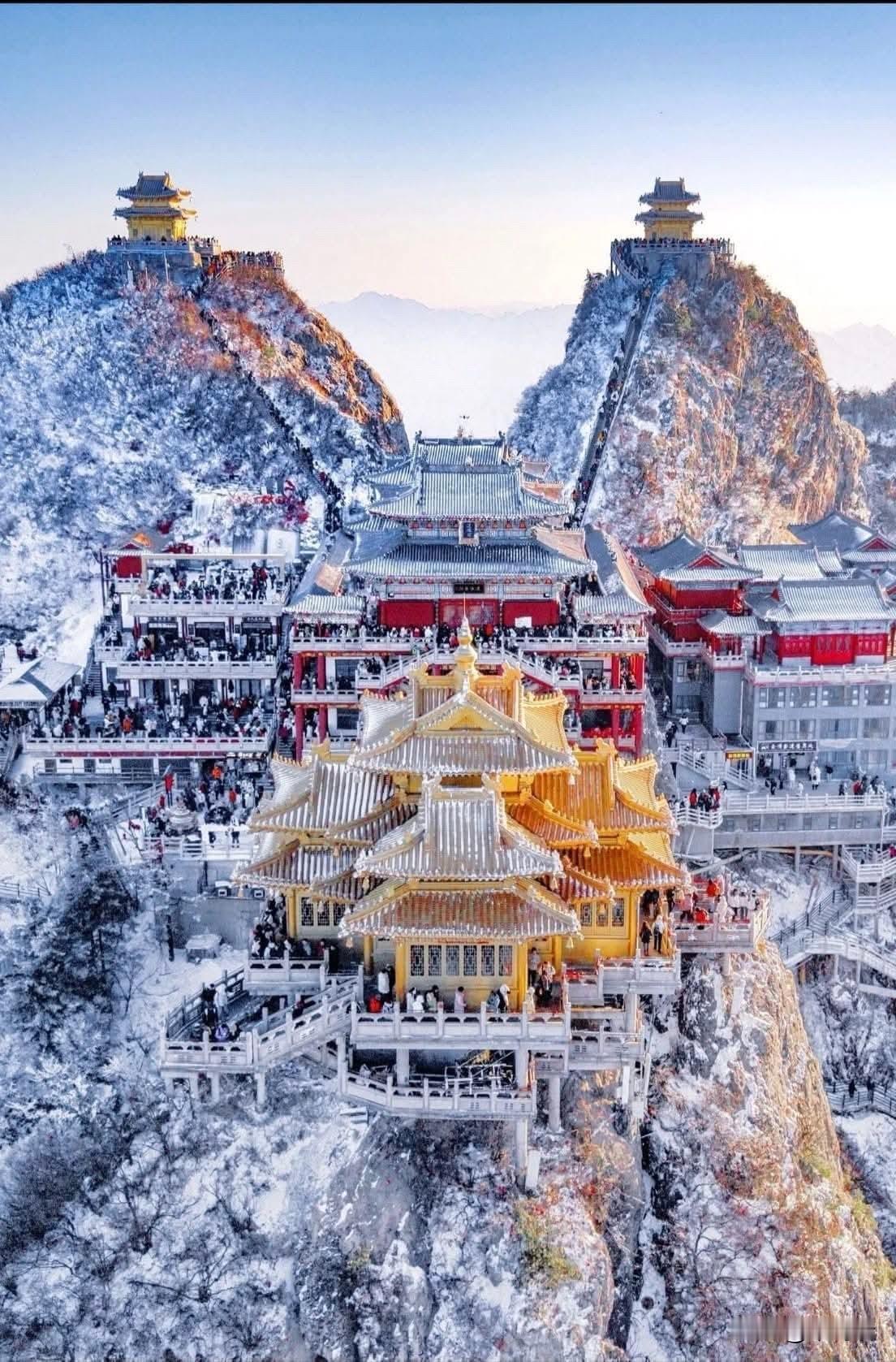河南省洛阳市的老君山冬季雪景图，画面展示了白雪皑皑的山峰和金碧辉煌的道教建筑群，