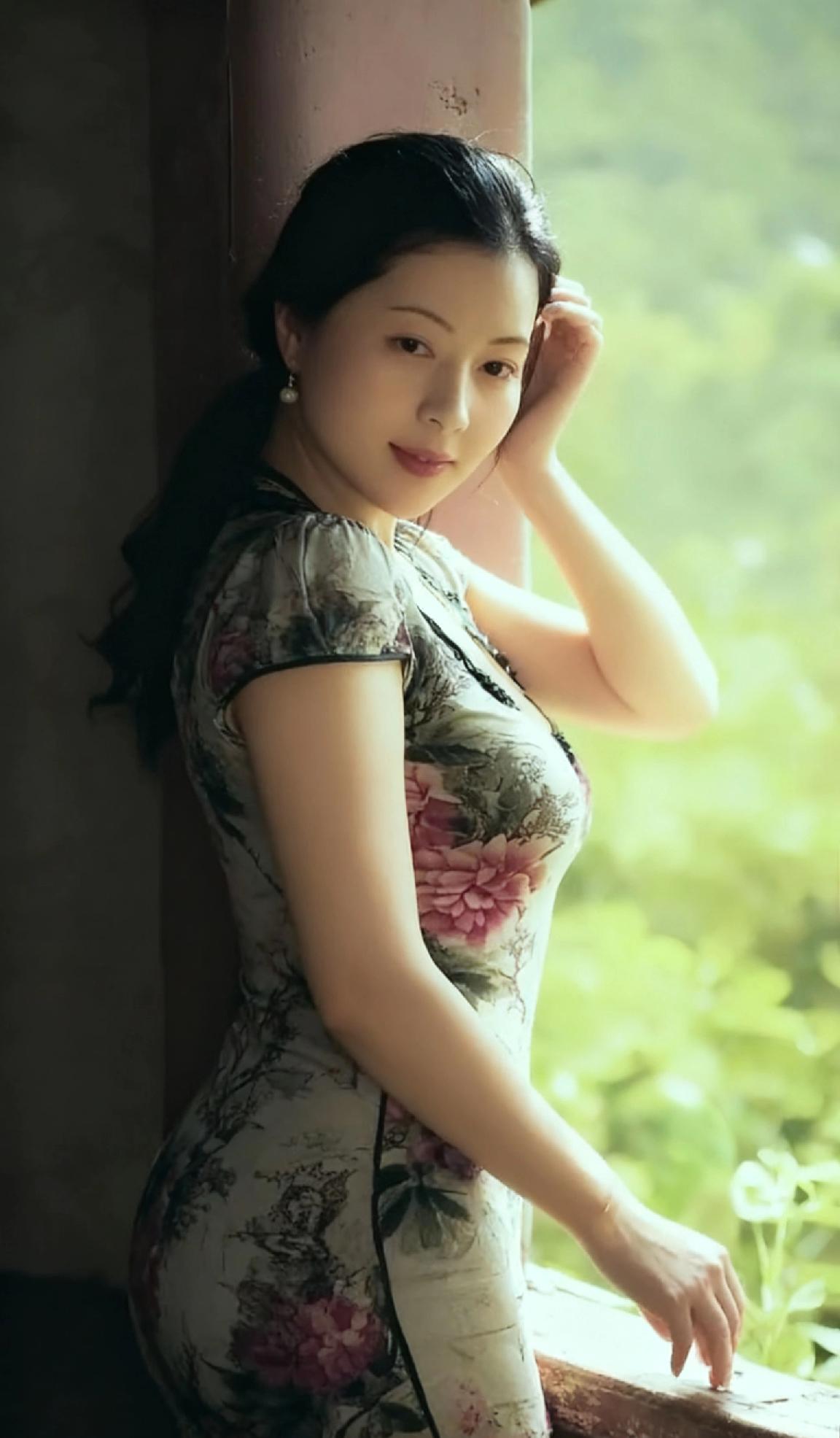 她身着水墨风旗袍，牡丹晕染间尽显东方气韵，乌发如瀑，耳饰轻摇，倚栏时腰肢纤细，眼