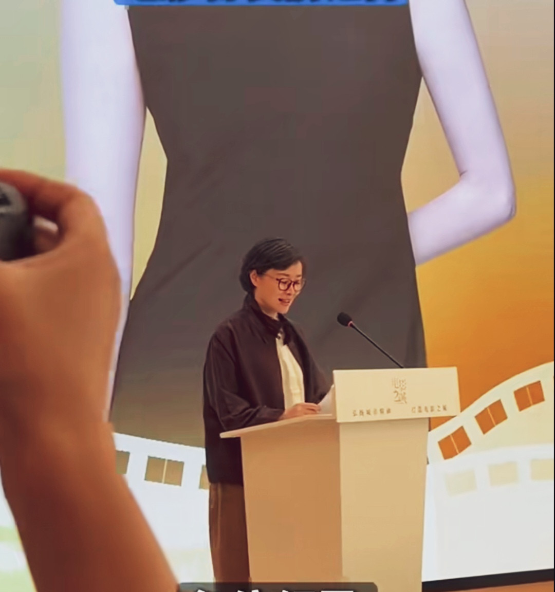 吴越线下论坛发言现场。利落短发，一副红框眼镜，低调素雅的穿搭，捧着稿件娓娓道来，气质沉静温润，知性气