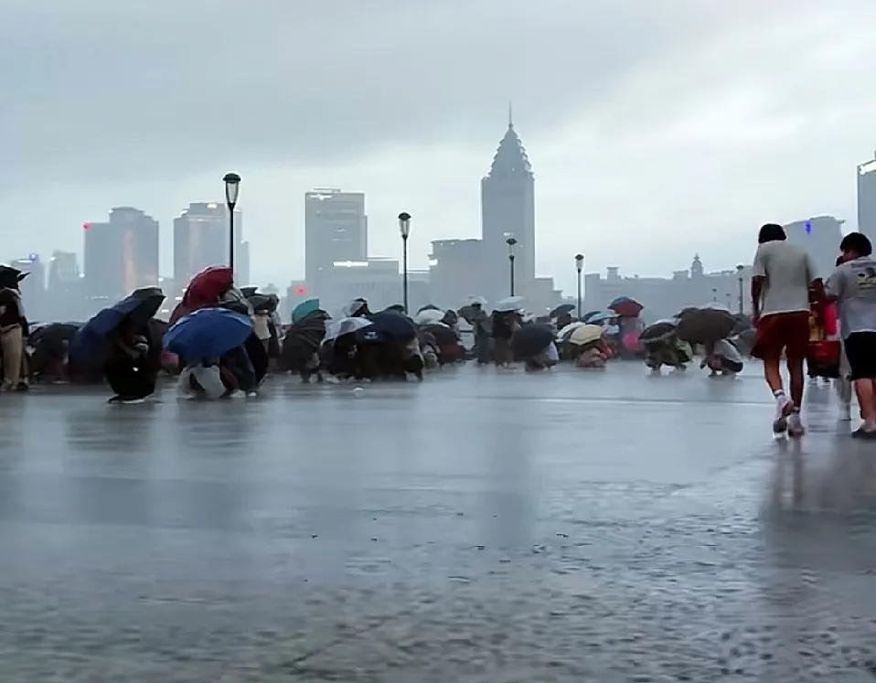 这是上海外滩游客突然遇到的下暴雨的景象，游客们扎堆蹲到地上，躲到伞子下面，而且都