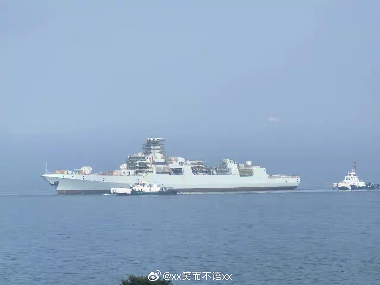 大连造船厂一艘055型正在转移舾装泊位，由拖船拖动，上层建筑还有大量脚手架。这是